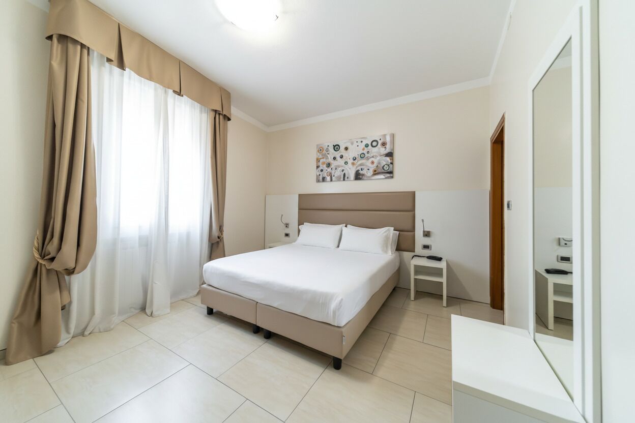 Un dormitorio con cama, cortinas, una mesita de noche y un cuadro en la pared.
