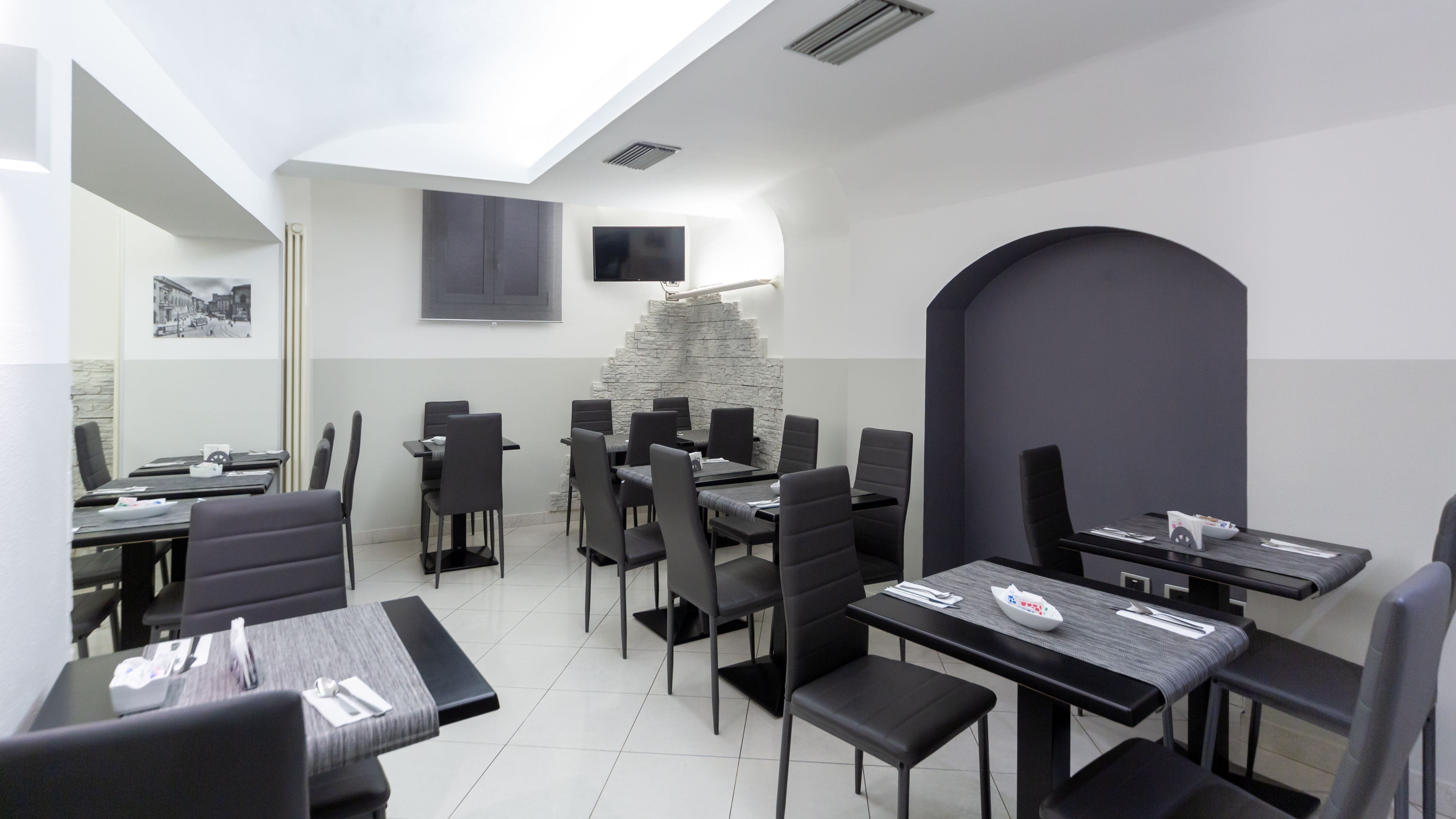 Un comedor moderno con varias mesas y sillas, un muro decorativo de piedra y un televisor de pantalla plana montado en la pared.