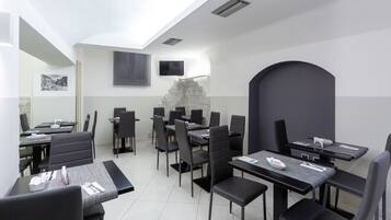 Un comedor moderno con varias mesas y sillas, un muro decorativo de piedra y un televisor de pantalla plana montado en la pared.