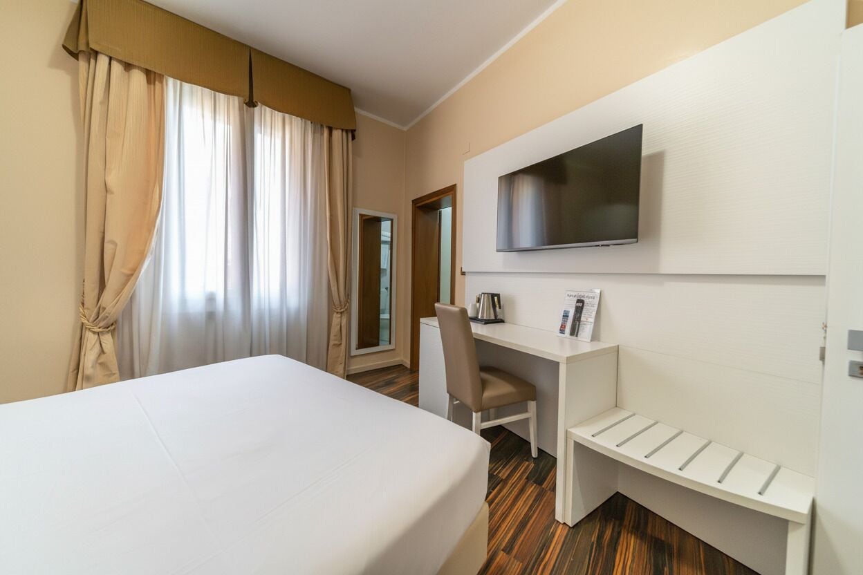 Ein Hotelzimmer mit Bett, Schreibtisch, Stuhl, Fernseher und einem kleinen Regal.