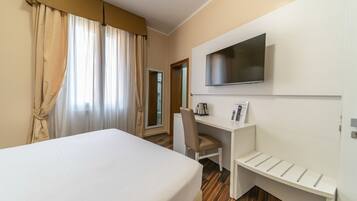 Ein Hotelzimmer mit Bett, Schreibtisch, Stuhl, Fernseher und einem kleinen Regal.