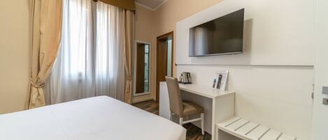 Une chambre d’hôtel avec un lit, un bureau, une chaise, une télévision et une petite étagère.