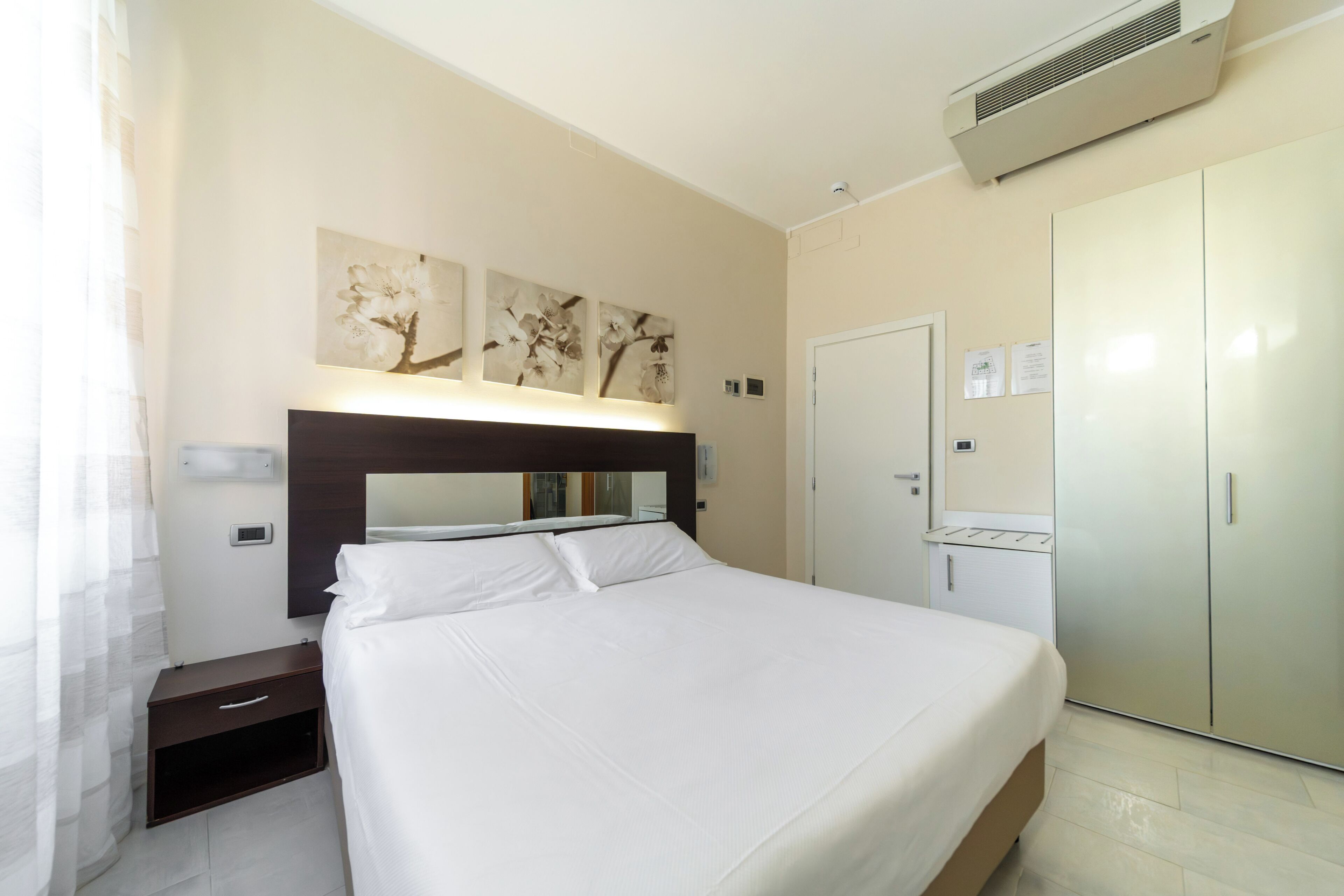 Een hotelkamer met een bed, nachtkastje, kledingkast en een wandairconditioner.