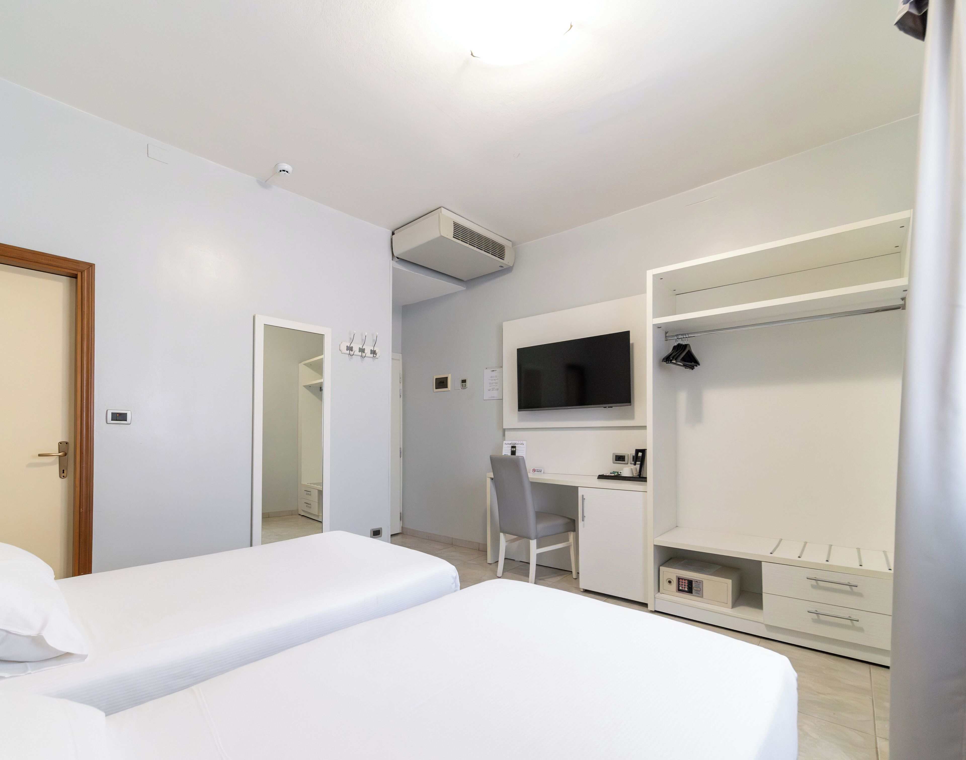A hotel room with two beds, a desk, a TV, and a wardrobe.