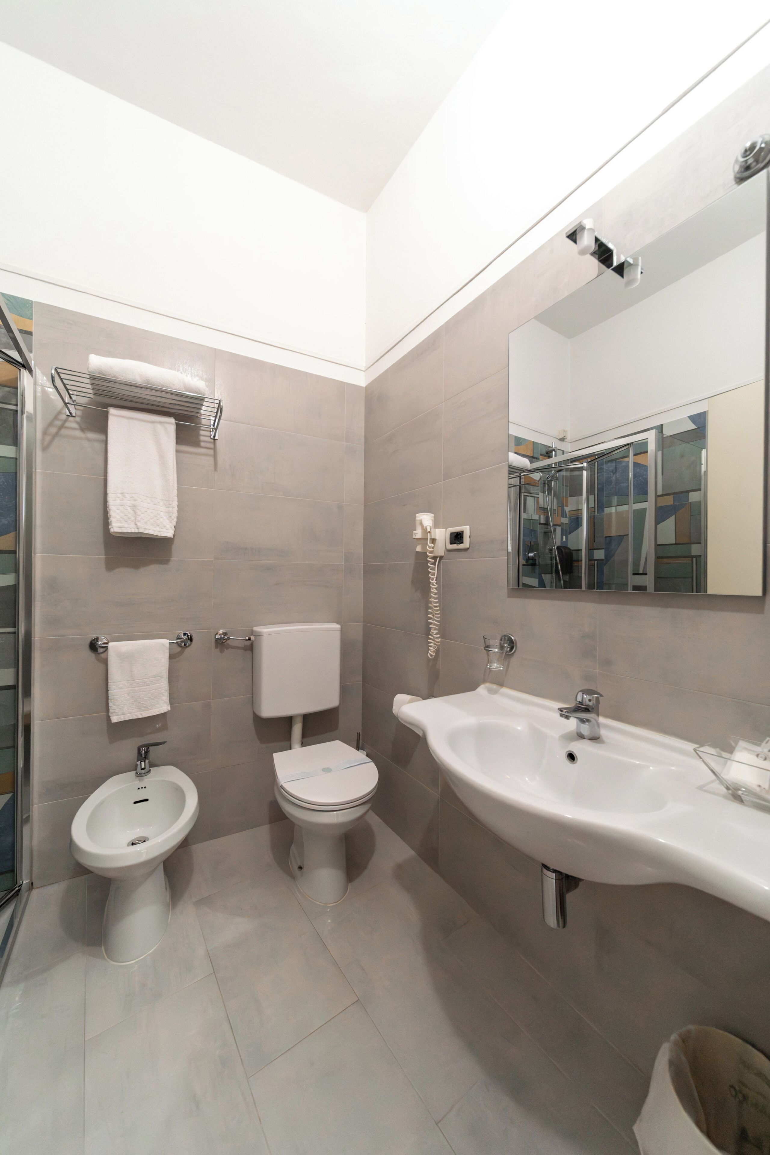 A modern bathroom with a bidet, toilet, sink, and a mirror.