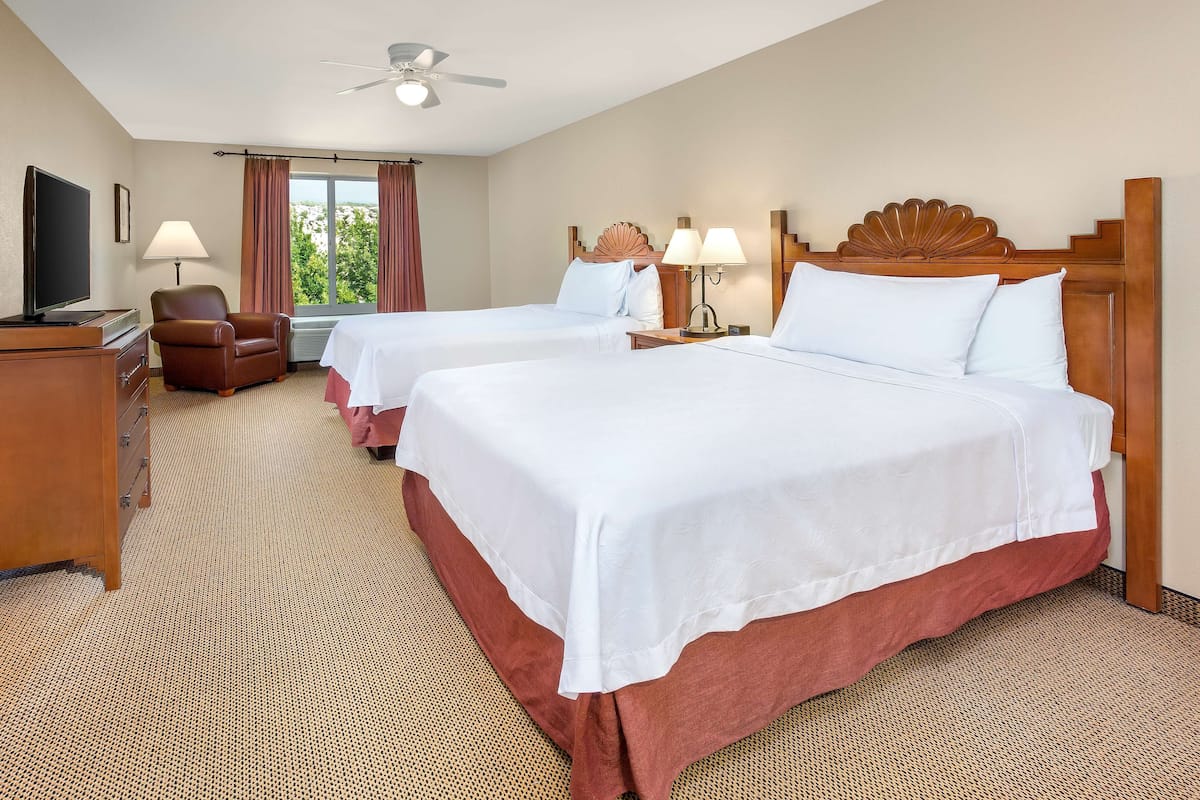 A hotel room with two beds, a TV, a desk, and a chair.