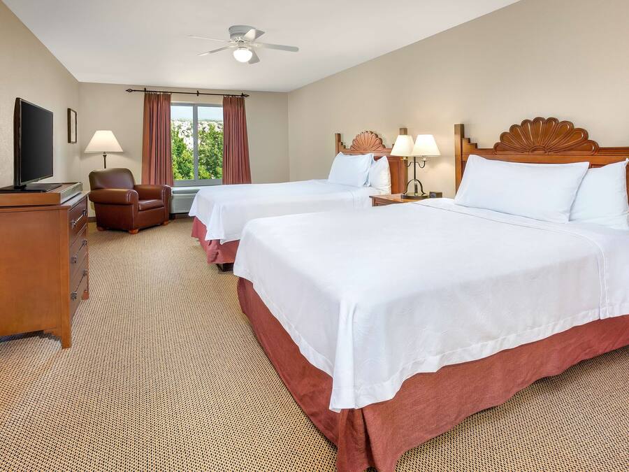 Ein Hotelzimmer mit zwei Betten, einem Fernseher, einem Schreibtisch und einem Sessel.