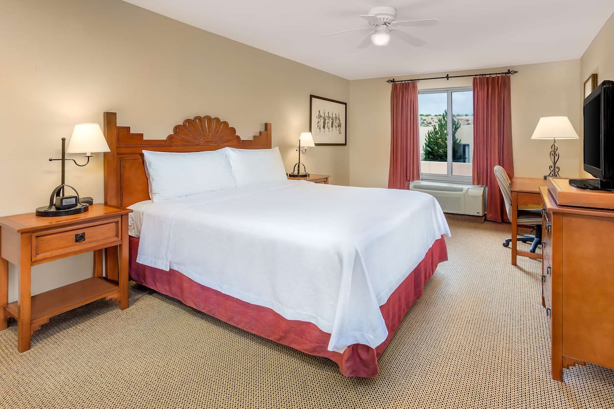 A hotel room with a large bed, two bedside tables, a desk with a chair, a television, and a window with curtains.