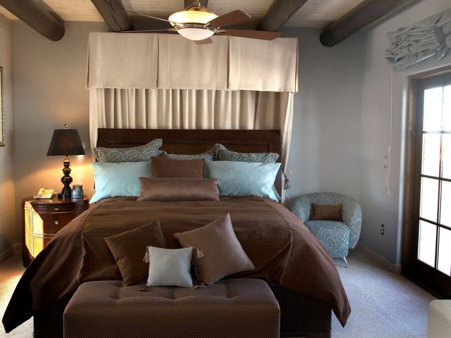 Una camera da letto con un letto grande, un comodino con una lampada, una sedia e una finestra con tende.