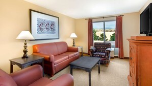A hotel room with a sofa, armchair, a small table, a cabinet, a television, and a large window with curtains.