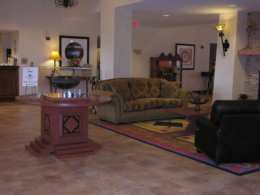 Un hall d’entrée avec une table ronde, un canapé et un fauteuil noir. Il y a un panneau sur le mur et une lampe sur la droite.