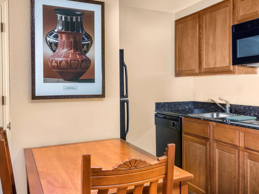 A compact kitchen with wooden cabinets, a microwave, a dishwasher, and a framed picture of a vase on the wall.