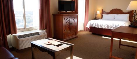 A hotel room with a bed, a TV on a wooden cabinet, a desk, a chair, and a window with curtains.