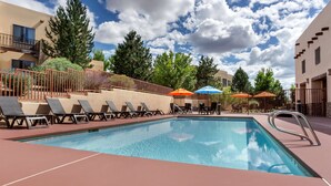 A swimming pool with lounge chairs and umbrellas, surrounded by buildings and trees.