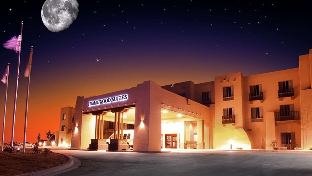 A hotel with a sign reading "Homewood Suites" at night, featuring a large moon in the sky.