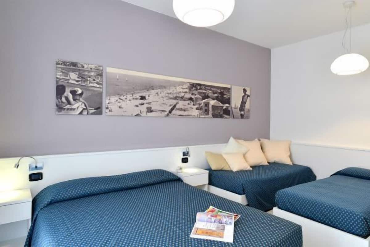 A hotel room with two beds, a nightstand, a wall-mounted light fixture, and a large photo collage on the wall.