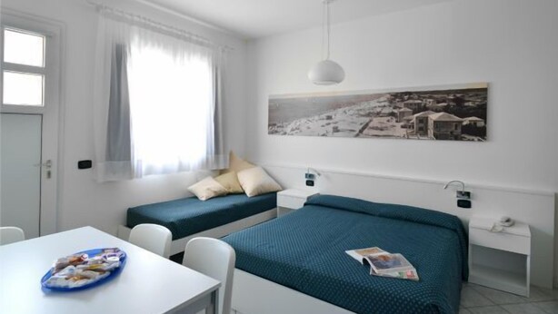 A small, clean room with two single beds, a white desk, and a window with sheer curtains. - Residence Progresso (Jesolo)