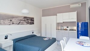 A bedroom with a bed, a small bedside table, a nightstand, a window, and a wall-mounted air conditioner. - Residence Progresso (Jesolo)