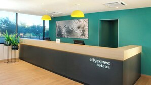 A reception desk with a sign reading "cityexpress hotels" and a large window with a view of trees. - City Express by Marriott Reynosa (Reynosa)