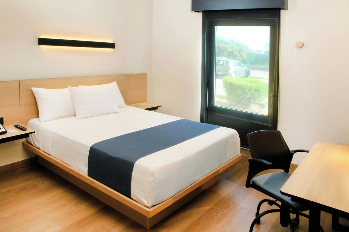 A hotel room with a bed, bedside table, chair, and a window with a view of the outside.