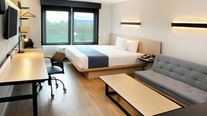 A modern hotel room with a bed, sofa, desk, and a large window offering a view. - City Express by Marriott Reynosa (Reynosa)