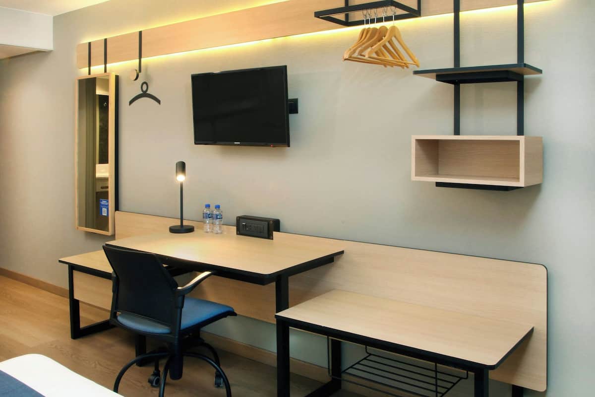 A modern hotel room with a desk, chair, and a flat-screen TV mounted on the wall.