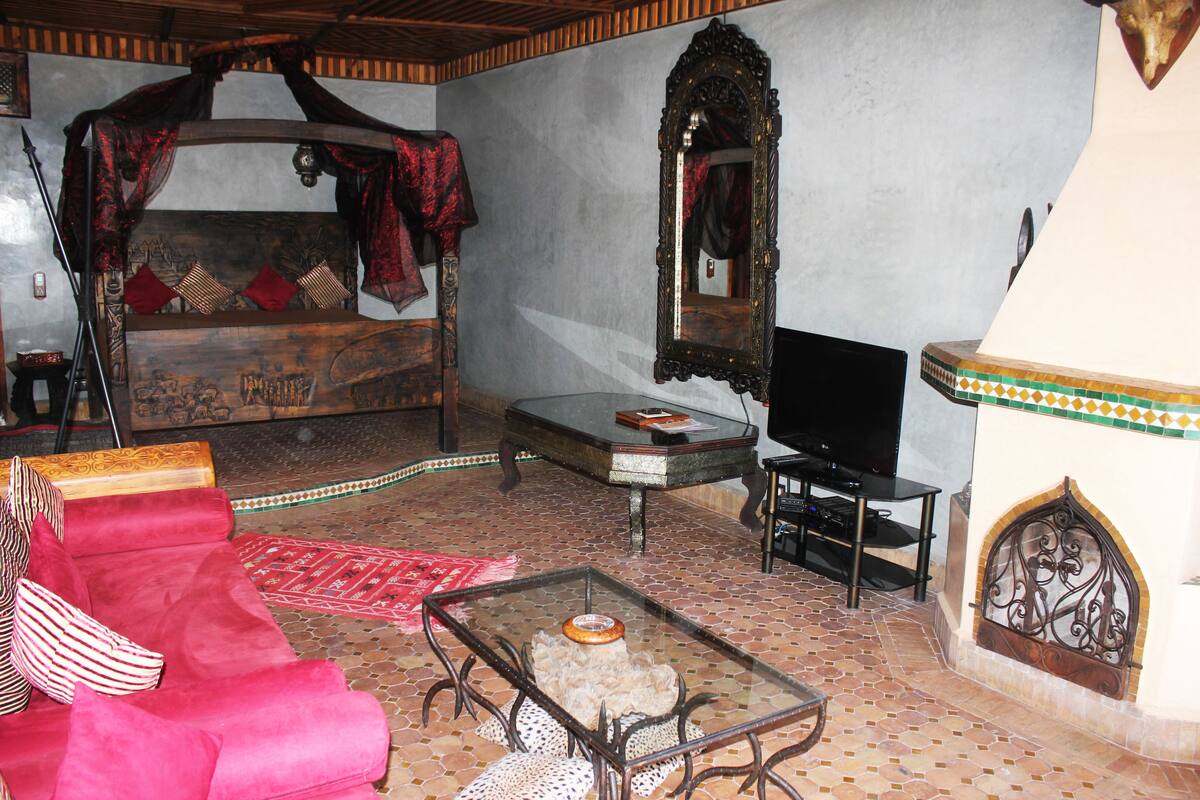 Une chambre avec un lit, un téléviseur, une table basse en verre et un tapis à motifs.