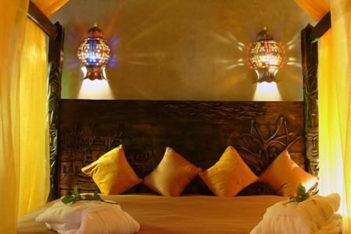 Une chambre avec un lit sous un dais, deux lampes fixées au mur et un plafond décoré de motifs.