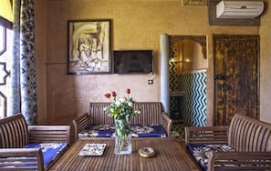 Une pièce avec une table en bois, des chaises, un vase de fleurs, un tableau et un téléviseur.