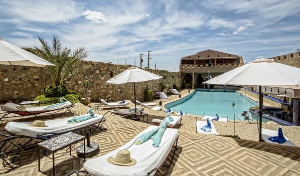A poolside area with sun loungers, umbrellas, and a stone wall. - Kasbah Le Mirage (Marrakech)