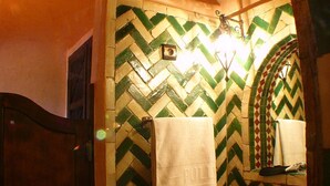 A bathroom with a herringbone patterned tile wall, a wooden door, a sink with a gold faucet, and a towel hanging on the wall. - Kasbah Le Mirage (Marrakech)