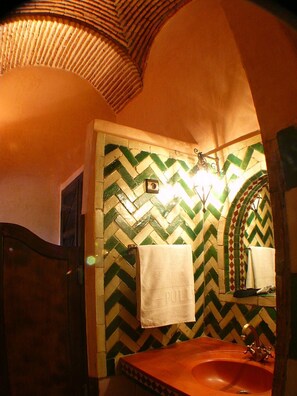 A bathroom with a herringbone patterned tile wall, a wooden door, a sink with a gold faucet, and a towel hanging on the wall. - Kasbah Le Mirage (Marrakech)