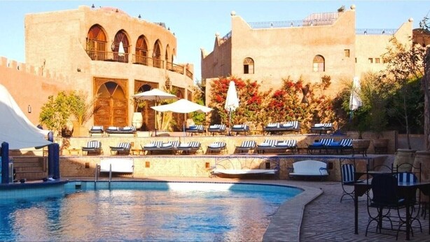 A pool area with lounge chairs and umbrellas, surrounded by a fortified building with arched windows and balconies. - Kasbah Le Mirage (Marrakech)