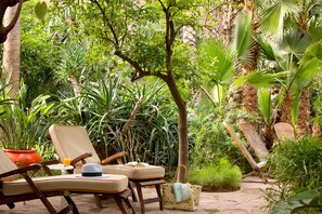A garden with lounge chairs, a table with a drink, and a handbag. - Les Jardins De La Medina (Marrakech)