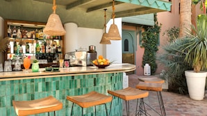 Una zona de bar con un mostrador de baldosas verdes, lámparas de mimbre colgantes y taburetes de madera.