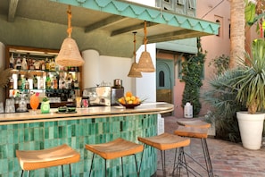 Una zona de bar con un mostrador de baldosas verdes, lámparas de mimbre colgantes y taburetes de madera.