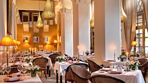 Un restaurante con varias mesas dispuestas para comer, con sillas de mimbre y manteles blancos.