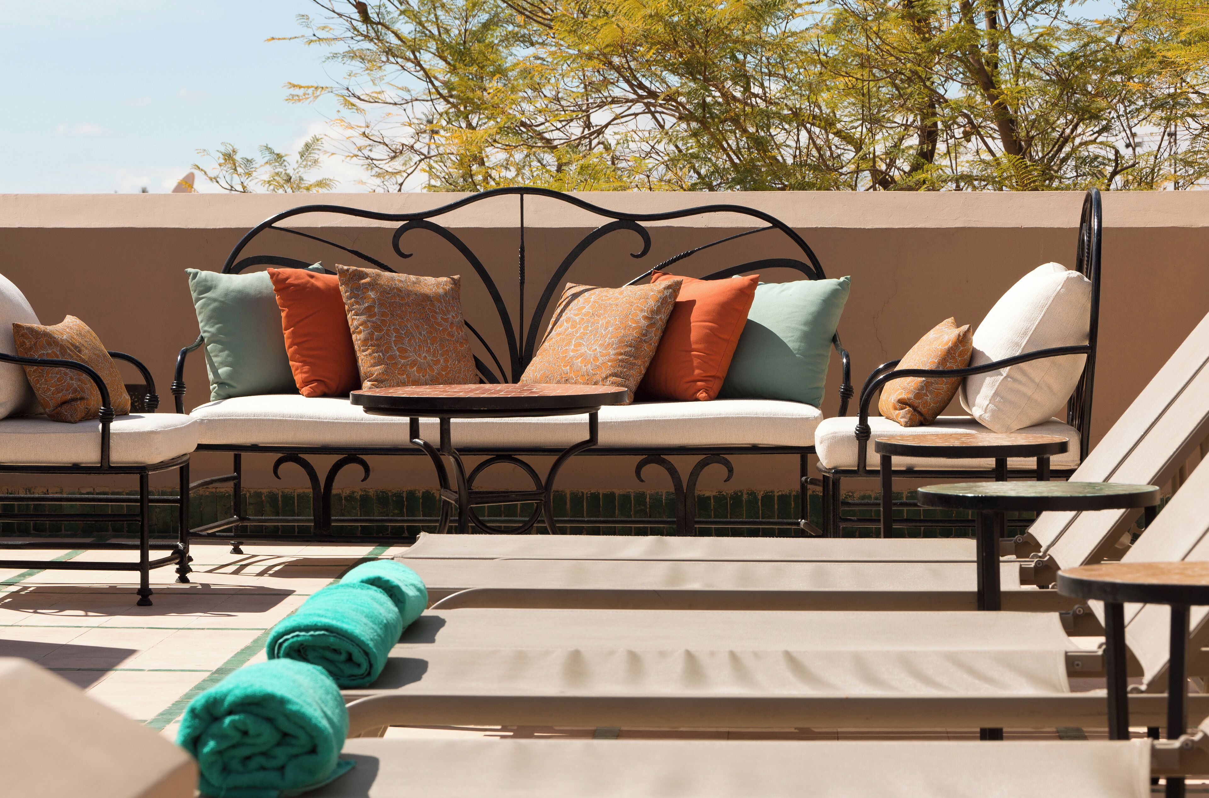 A rooftop lounge area with sun loungers and a seating area with cushions and a table.