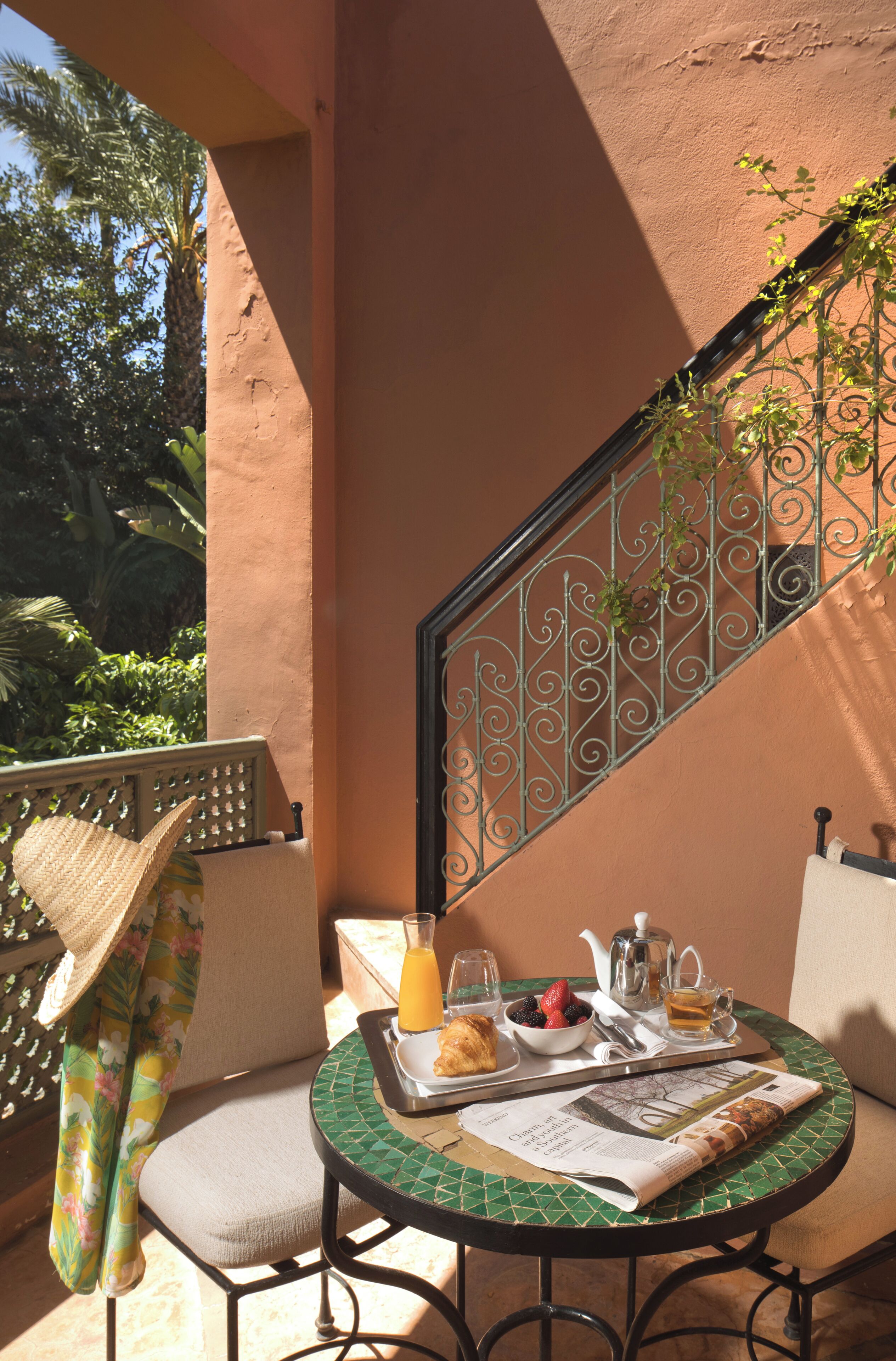 Un balcón con una mesa dispuesta para el desayuno, que incluye un periódico, una tetera y una bandeja con comida y bebidas.