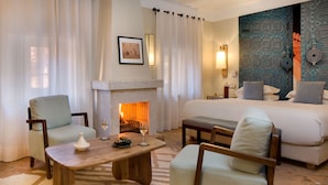 Una habitación de hotel con chimenea, una cama, dos sillones, una mesa de centro y un tapete estampado.