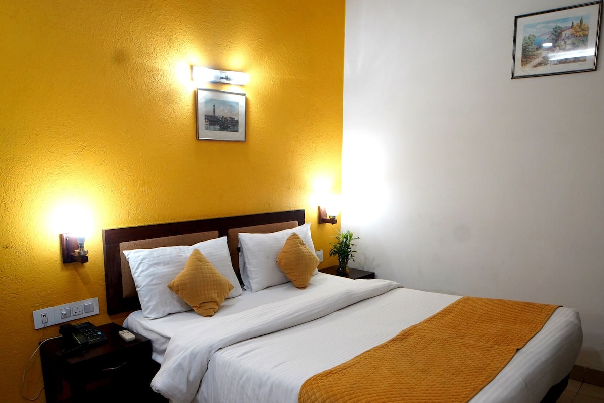 A hotel room with a large bed, a nightstand, a wall-mounted lamp, and a framed picture on the wall.