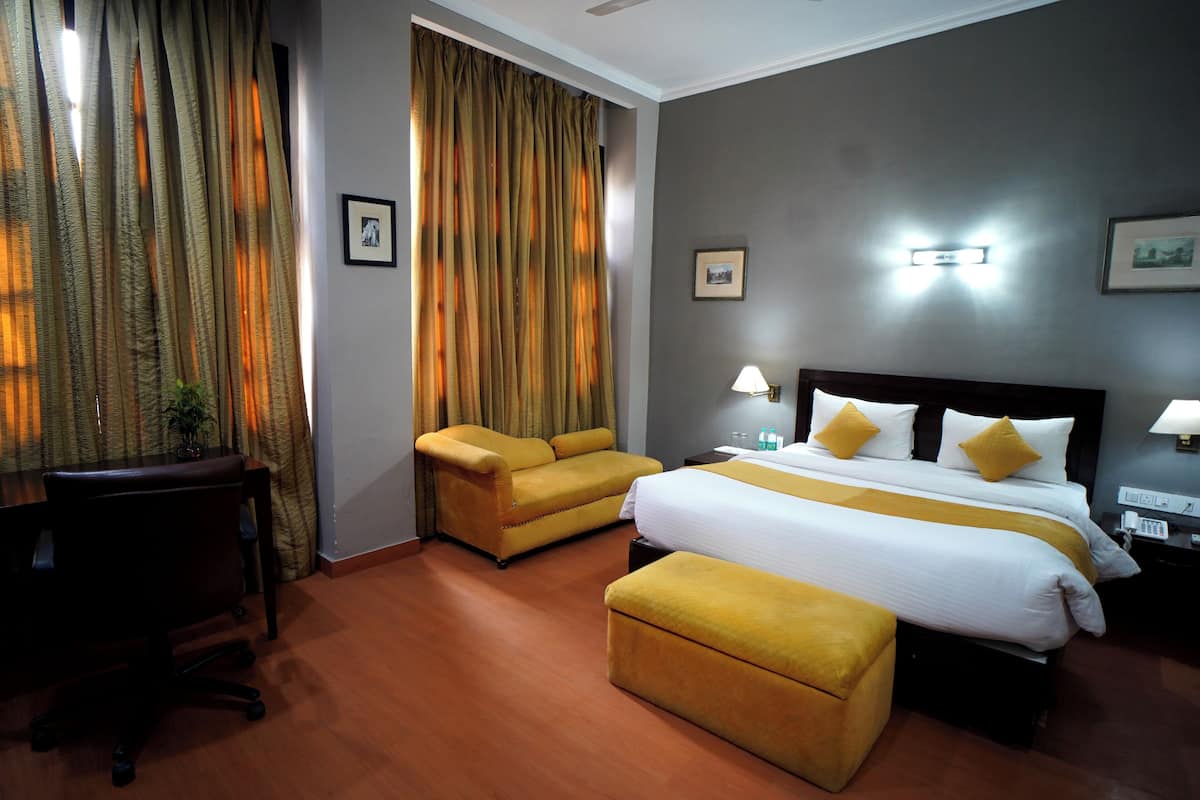 A hotel room with a bed, two yellow armchairs, a desk, and a small table.