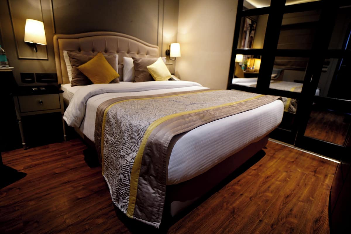 A hotel room with a large bed, two bedside tables, a nightstand, and a wardrobe.