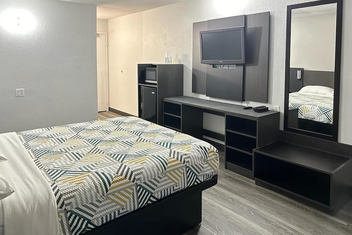 A modern hotel room with a bed, a TV mounted on the wall, a desk, and a mirror.