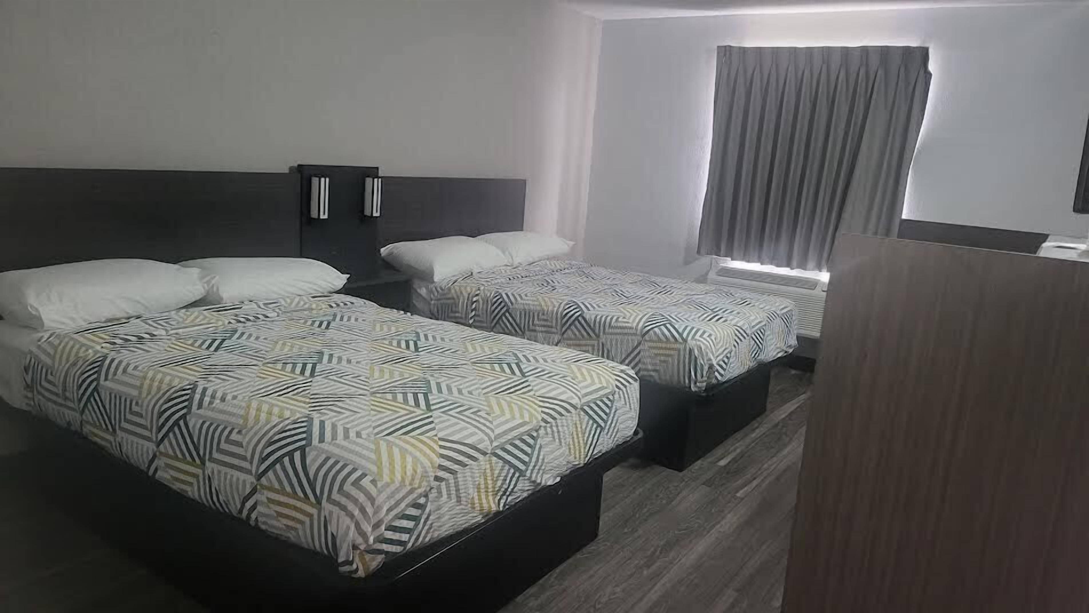 A hotel room with two beds, each with patterned bedding, a nightstand, a wardrobe, and a window with curtains.
