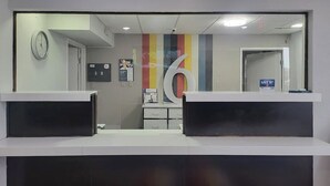 A reception area with two counters, a clock, and a colorful vertical stripe design on the wall. - Motel 6 Omaha, NE (Omaha)