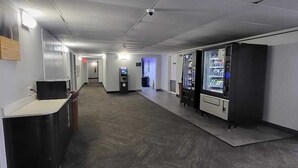 A corridor with vending machines, a reception desk, and a security camera. - Motel 6 Omaha, NE (Omaha)