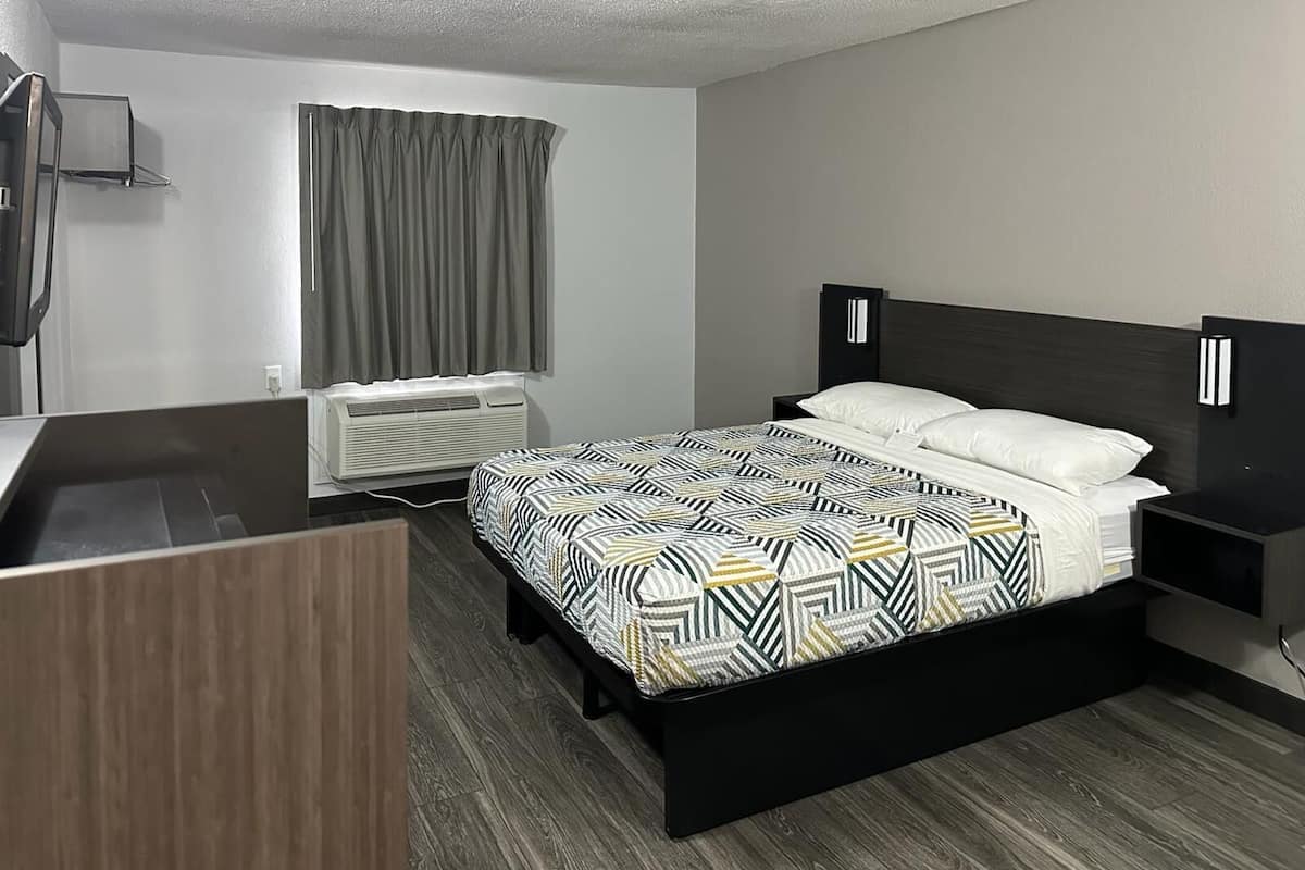 A modern hotel room with a bed, bedside tables, a desk, and an air conditioning unit.