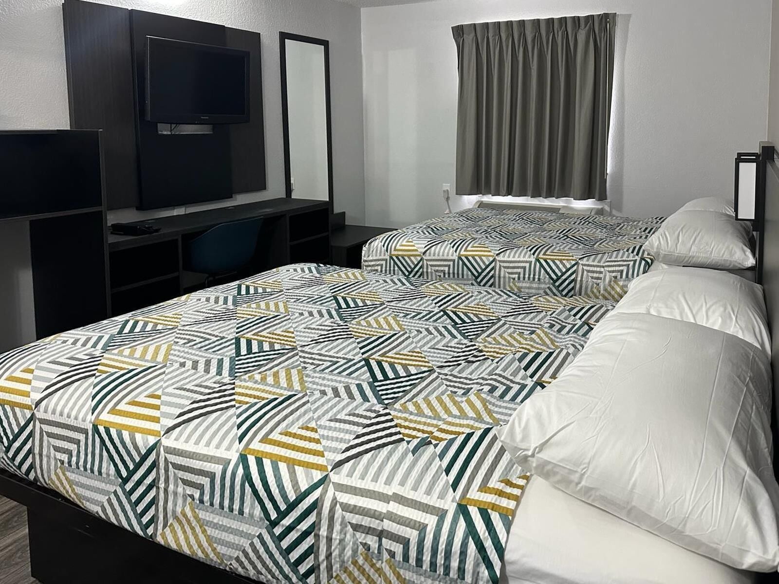 A hotel room with two beds, a desk, a chair, a television, and a window with curtains.