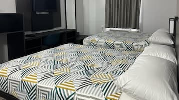 A hotel room with two beds, a desk, a chair, a television, and a window with curtains.